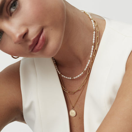 model's decollétage wearing a pearl and gold seed choker necklace, a gold paperclip necklace and a gold friendship disc charm on a gold belcher chain necklace